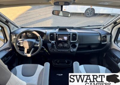 Interior view of a camper van cab: steering wheel on the left, central touchscreen, climate controls, and two front captain seats; SWART CAMPERS watermark in corner.