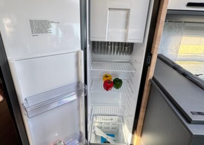 Open camper fridge with peppers on the middle shelf and a can of Fanta on the door shelf.