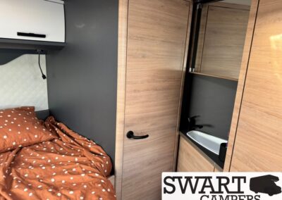 Bed with an orange polka-dot comforter next to dark wall and built-in wooden cabinets in a compact camper interior.