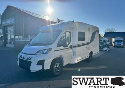 White motorhome on a dealership lot beside a workshop building, with Swart Campers branding in the corner. Unobstructed sunny day.