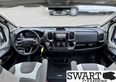 Interior cockpit of a camper van: steering wheel, central touchscreen, climate controls, gear lever, and two front seats; SWART CAMPERS watermark.