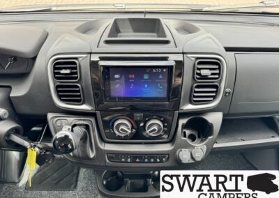 Van dashboard with a touchscreen infotainment system, two air vents, climate control dials, and a gear shift nearby.