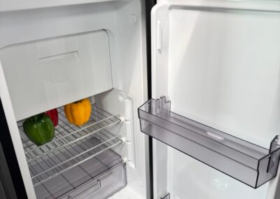 Open mini fridge in a camper with bell peppers on the rack and a can on the bottom shelf; Swart Campers watermark in corner.