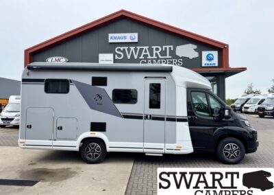 Side view of a grey and white motorhome parked in front of a Swart Campers building with a red roof and large SWART CAMPERS sign