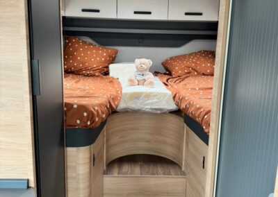 Twin bunk beds in a camper, orange polka-dot bedding, a teddy bear between them, with overhead cabinets above.
