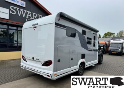 White KNAUS motorhome parked outside a Swart Campers dealership, with the Swart Campers sign visible in the background and other campers nearby.