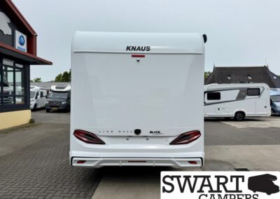 Rear view of a white KNAUS Live Wave caravan, with taillights and bumper visible, parked in a lot with other campers; SWART CAMPERS watermark in bottom-right.