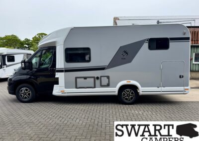 Side view of a gray and white motorhome with black cab, featuring a large side window and decorative graphic, parked on a paved lot near other campers.