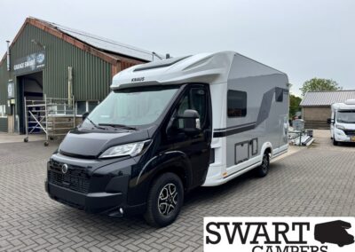 KNAUS motorhome with black cab and white body, parked in a brick-paved dealership lot.
