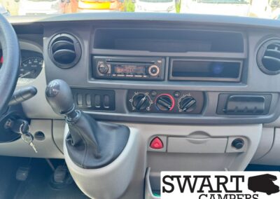 Interior of a van dashboard with manual gear lever, steering wheel, and center console housing the radio and climate controls; Swart Campers watermark in the bottom-right corner