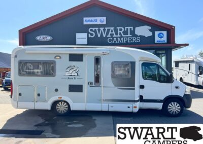 White Sun Ti motorhome parked in front of a Swart Campers dealership building with logos on the dark blue facade and clear blue sky.