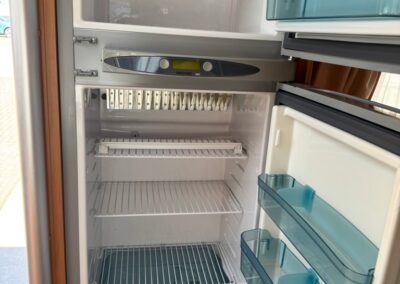 Camper refrigerator with freezer on top and empty shelves; blue bin at bottom and door shelves with blue bins visible.