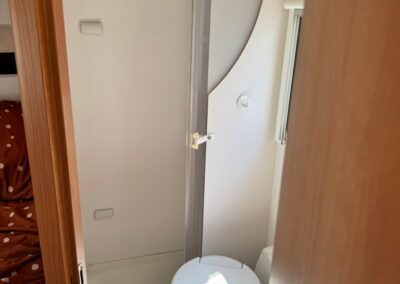 Compact camper bathroom with a toilet and curved shower stall seen from the doorway.