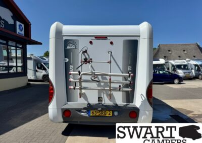 Rear view of a white camper van with a bike rack on the back, parked among other campers at a dealership lot.