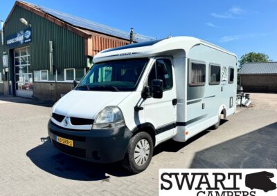 White Knaus camper van parked outside a workshop building labeled 'Garage Swart'; clear blue sky, front license plate 63-SRB-2 visible.