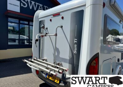Rear view of a white motorhome with a bike rack mounted on the back, parked outside a dealership.