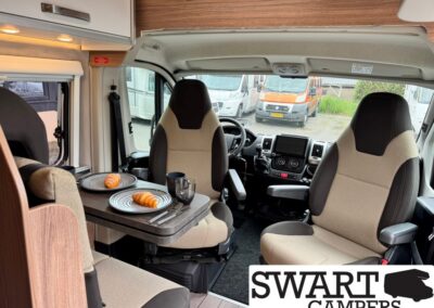 Interior of a camper van with a small dining table set for two, croissants on plates and a mug.