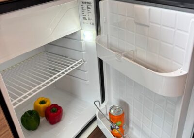 Open mini fridge in a camper with green, yellow, and red bell peppers on the shelf and a can resting on the door rack.