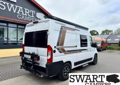 White camper van with brown geometric graphics parked outside Swart Campers showroom, with an orange van in the background.