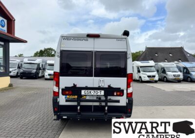Rear view of a white WENSBERG CaraBus camper van with a bike rack mounted on the back, parked among other motorhomes at a dealership lot.