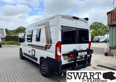 White camper van with geometric brown and gray graphics, parked on a paved lot; rear bike rack and European license plate visible, branding says WEINSBERG on the back and side.