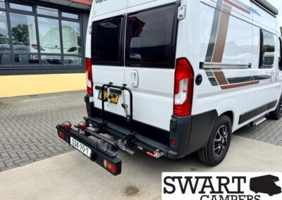 White camper van with a rear-mounted bike rack, parked in a lot; brown geometric decals along the side and a SWART CAMPERS logo in the bottom-right corner.