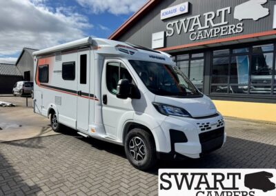 White motorhome parked outside a Swart Campers dealership, with a large sign and windowed showroom in the background.