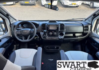 Driver's-seat view of a Fiat camper interior: steering wheel, central touchscreen, gear lever, and dashboard controls; SWART CAMPERS watermark.