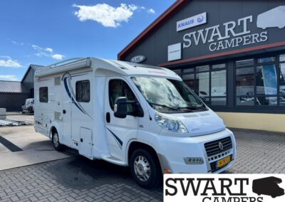White motorhome parked outside a Swart Campers showroom on a sunny day.