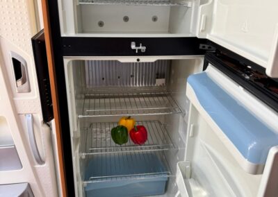 Compact RV refrigerator with three peppers (yellow, green, red) on a middle rack and a blue bin on the bottom shelf.