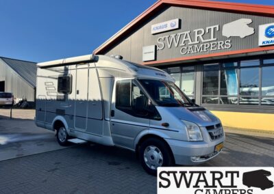 Silver motorhome parked outside a Swart Campers dealership building with logo and large windows in the background.