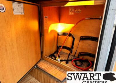 Open camper van storage compartment with hoses and straps inside a wood-paneled cabinet.