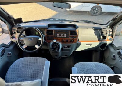 Front interior of a Ford camper van: steering wheel, gear shift, radio, and wood-trim dashboard.