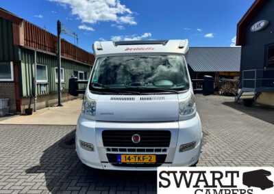Front view of a white Dethleffs camper van parked in an industrial yard under a blue sky.