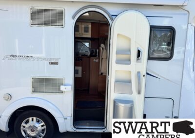 White motorhome with the entry door open, revealing a kitchenette and seating area inside the camper van.