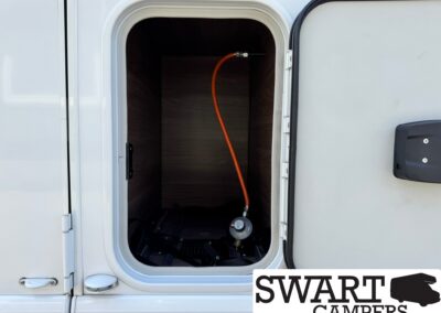 Open exterior storage compartment of a camper with an orange hose inside.