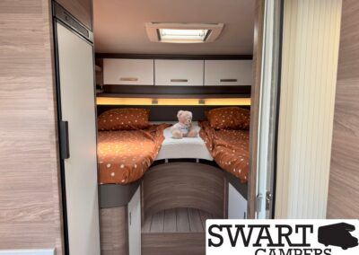 Camper bunk bed area with orange polka dot bedding, a teddy bear, white overhead cabinets, and a skylight.
