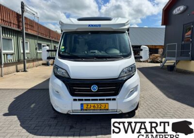 Front view of a white camper van with license plate ZJ-632-J, parked in a lot beside industrial buildings under a blue sky.
