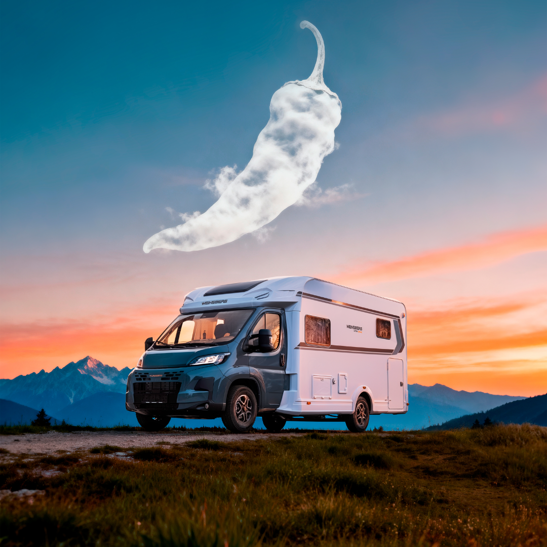 Camper van parked on a hill at sunset with a giant cloud shaped like a chili pepper in the sky, mountains in the distance.