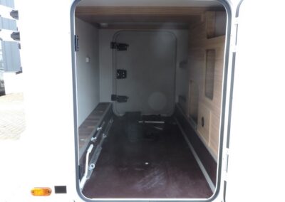 Open cargo/storage bay of a white camper, interior with wood paneling and a few items on the floor.