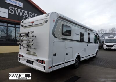 White motorhome with a mounted bike rack at the rear, parked outside a dealership with 'SWART CAMPERS' signage in the background.