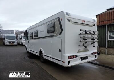 Rear view of a white motorhome with a mounted bike rack on the back, parked in a dealership lot with other campers nearby.