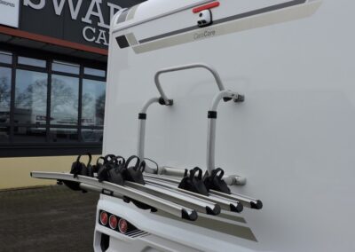 Rear view of a white caravan with a multi-bike rack mounted on its back, outside a dealership with 'SWART CAMPERS' signage.
