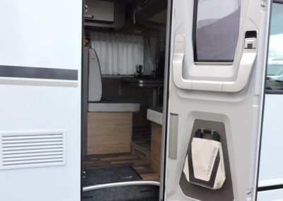 Open motorhome doorway with two-step entry, showing a compact kitchen and seating area inside the camper van.