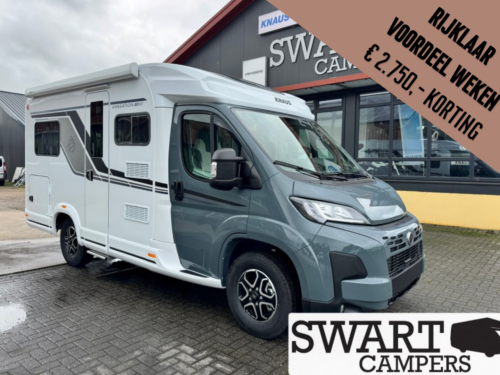 White and gray motorhome parked outside a camper dealership with Swart Campers signage nearby.