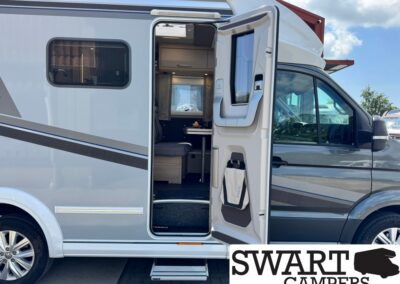 Camper van with the side door open, revealing a compact living area with seating inside and a small table viewable from the doorway