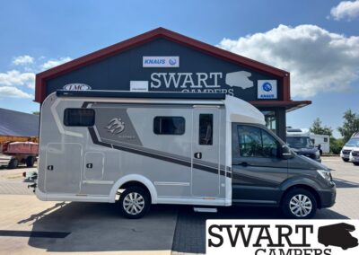 Side view of a silver-gray Motorhome with decorative graphics parked in front of a Swart Campers building.
