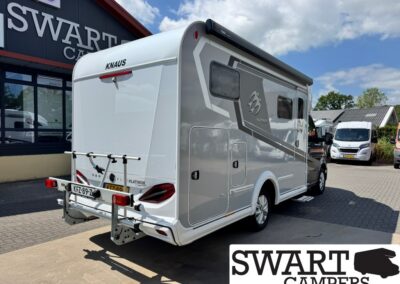 Rear three-quarter view of a white and gray Knaus Platinum motorhome parked outside a dealership, with a bike rack mounted on the back.