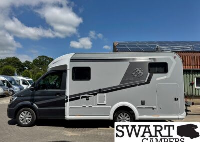 Side view of a grey and white motorhome parked in a lot, with a graphic design on its side and solar panels visible on a nearby roof.