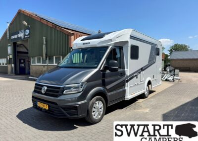 Grey and white Knaus motorhome parked on a paved lot outside a workshop with a 'Garage Swart' sign in the background, on a sunny day.